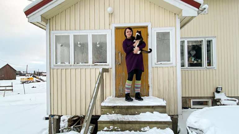 Nainen seisoo omakotitalon portailla kissa sylissään.