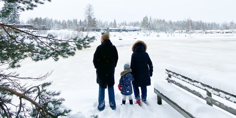 Isovanhemmat ja lapsenlapsi talvisen joen rannassa.