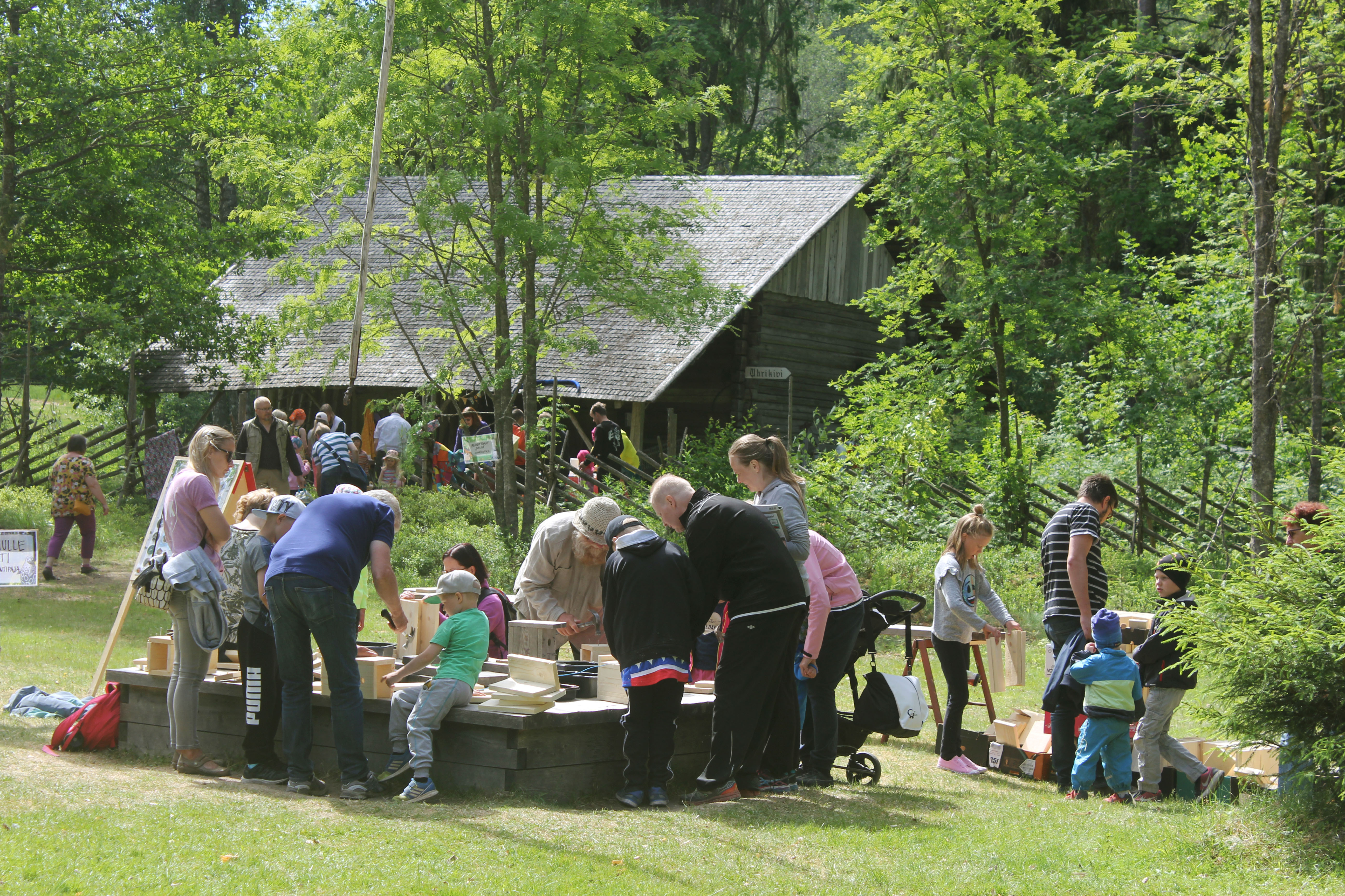 Kesänavaus tapahtumassa joukko kaikenikäistä yleisöä osallistuu linnunpönttöjen rakentamiseen keskellä museon pihaa.